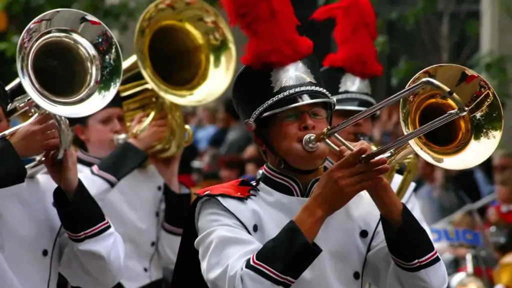 Group of marching band students in white uniforms playing trombone.