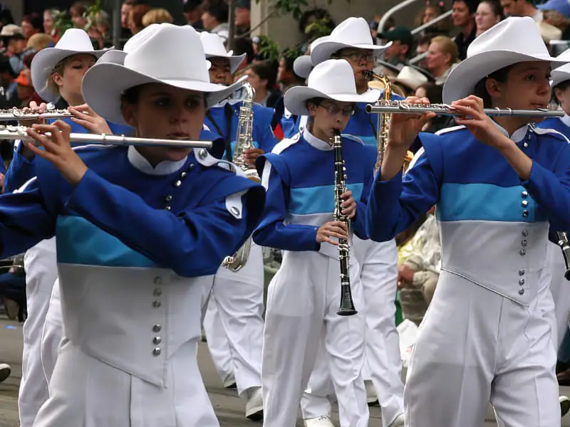 Marching band players wearing white and blue uniforms with cowboy hats