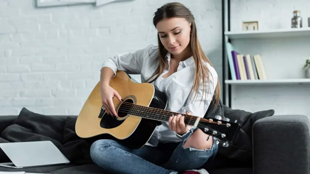 focused girl sitting on the couch playing the guitar