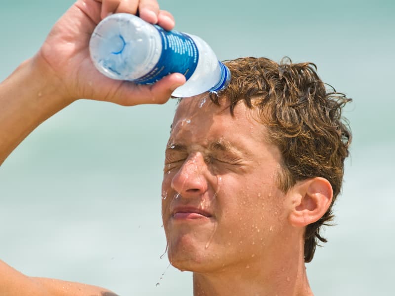 Boy dumping water on his head from a cold water bottle. 