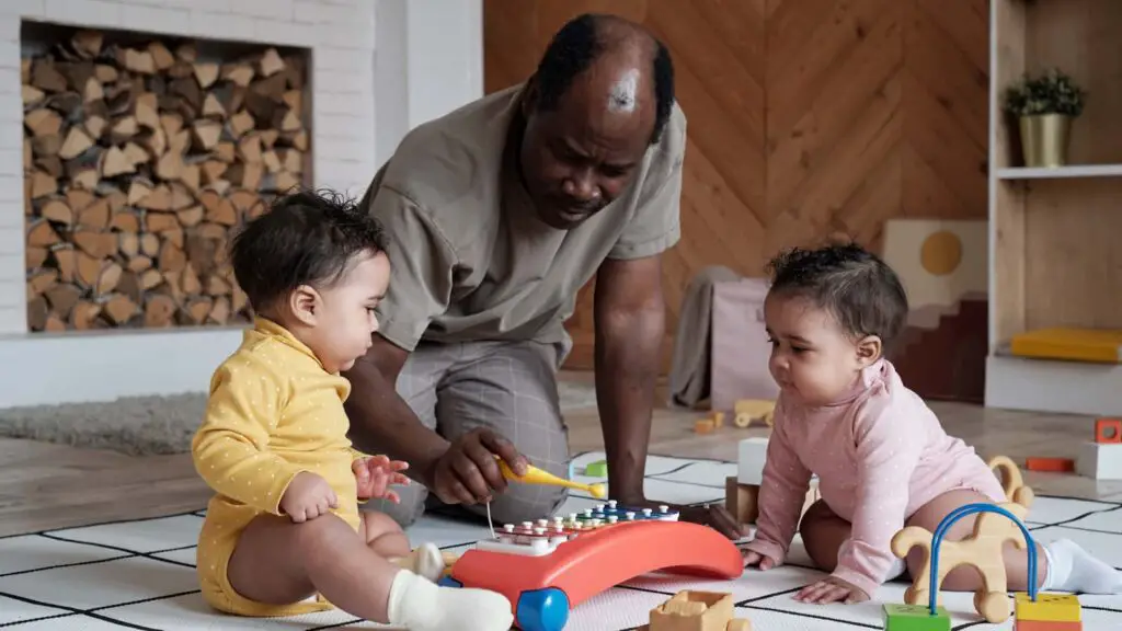 Father sitting with 2 babies on the floor playing the xylophone