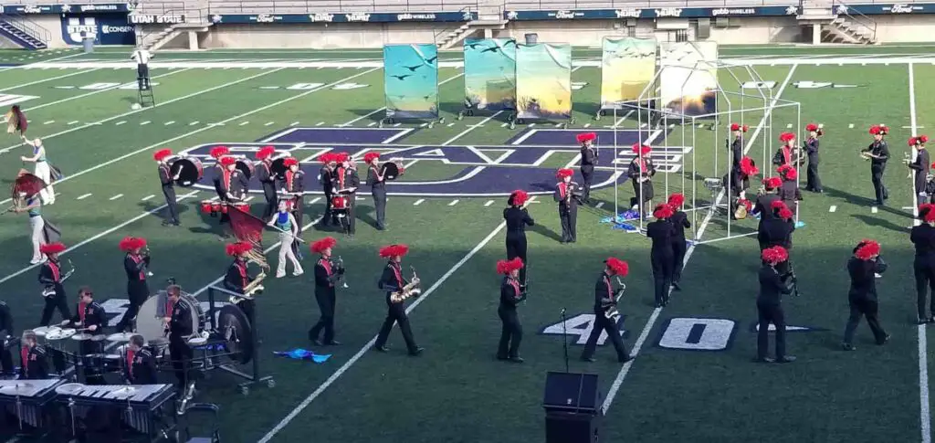 Marching band members performing at a competition in a college football stadium